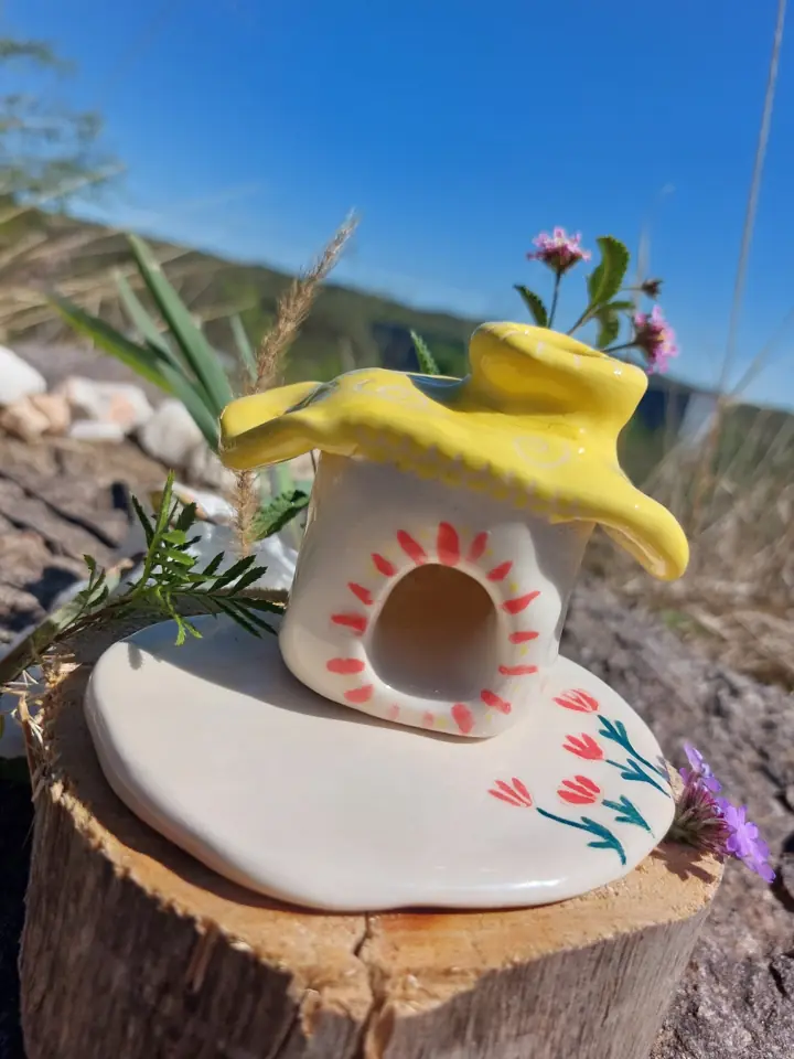 Casita amarilla de cerámica sobre una base con flores pintadas